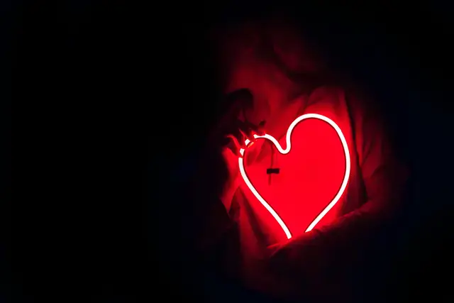 Silhouette of a person with a glowing red neon heart in the dark, symbolizing love